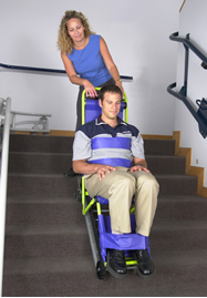 Colour photograph showing a Manual/Gravity Fire Evacuation Chair Device in operation. Transfer from a wheelchair to this type of device at the top of a staircase can be difficult and hazardous ... it can only travel down a staircase, using gravity (never up, against gravity !) ... and during horizontal travel, it is shaky and unstable. Click to enlarge.