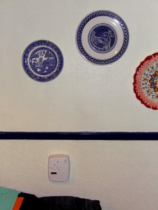 Colour photograph showing a battery-operated Ei Electronics Carbon Monoxide (CO) Detector, Model Ei206D, fixed (tamper proof) to the kitchen wall. Two of the hanging decorative plates are from France and Turkey. As for the third plate ... does anyone remember the Willow Pattern ? Photograph taken by CJ Walsh. 2011-01-12. Click to enlarge.
